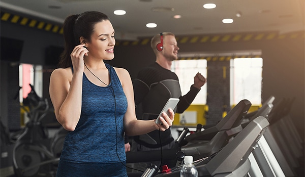 Young woman with smartphone running on treadmill in gym. Slim girl jogging in fitness club, listen mobile music. Healthy lifestyle concept, cardio training, copy space