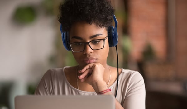 Focused african american girl student wearing headphones looking at laptop watching online webinar training course, serious mixed race woman learning english language on computer, internet e-learning
