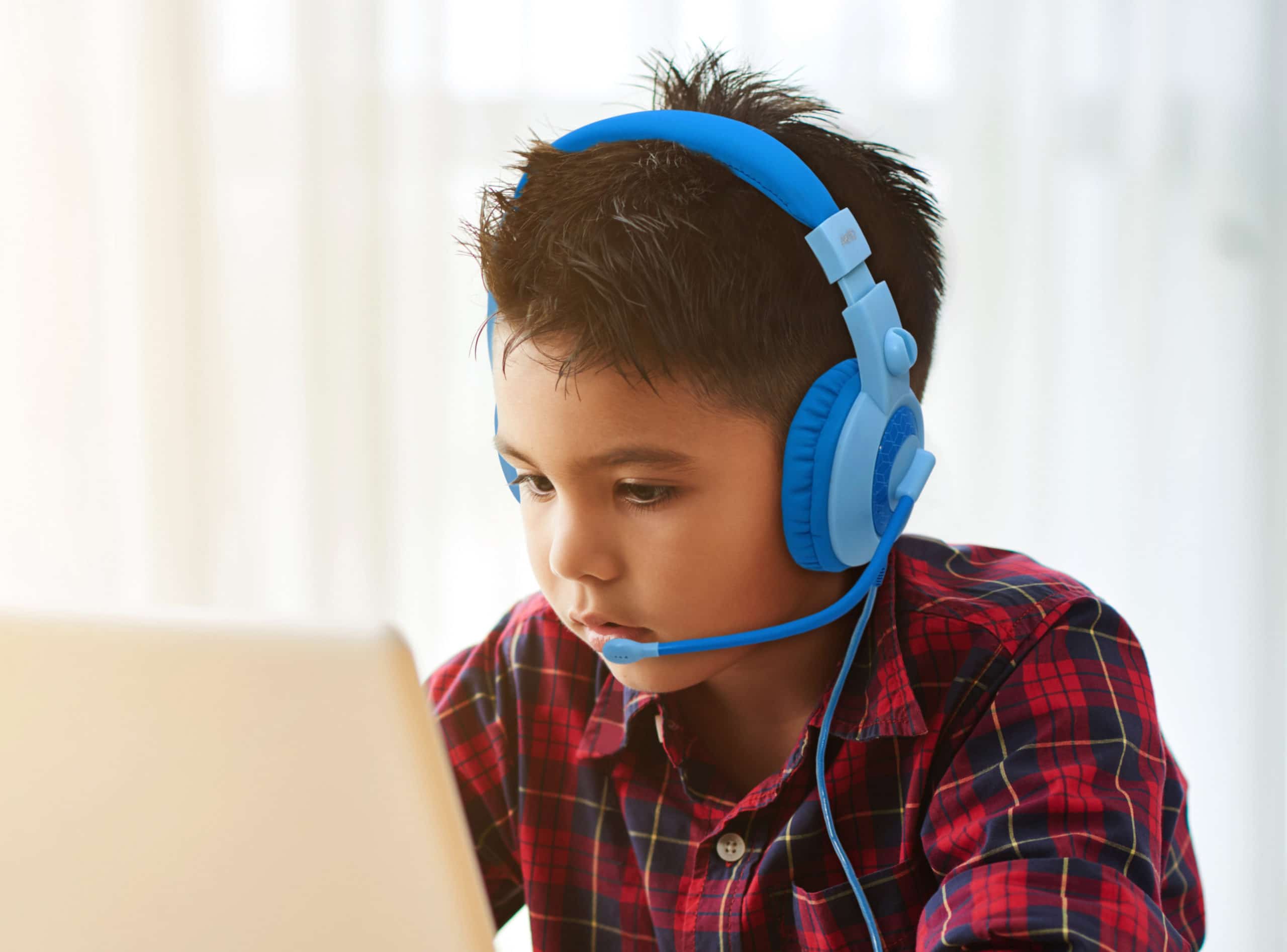 Cute little boy in headphones watching something on laptop at home